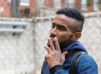 Young handsome African American man smoking cigarette in alley. Lips blowing smoke on blurred background. Portrait gangster smokes marijuana or cannabis. Portrait of a black guy smoking a cigarette.