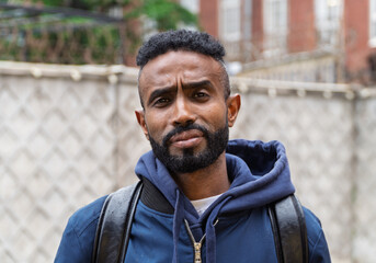 Portrait of a serious adult African American ethnicity man with a beard and glasses. A serious confident black guy a blue jacket posing. Portrait of a black man from Sudan on the blurred background. 