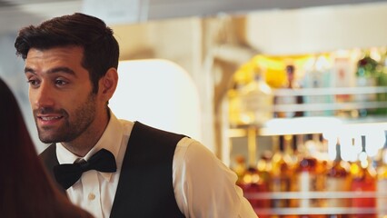 Smiling smart bartender providing excellent service to beautiful guest woman at back side vibrant nightlife party atmosphere in engaging lively conversation with VIP customer at nightclub . Vinosity.