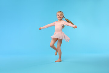 Fototapeta premium Cute little girl dancing on light blue background