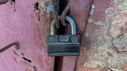 Close-up of an old padlock on the door, pink metal with scratches and rust. The lock is closed and covered in dust.