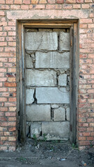 A broken door is patched with concrete blocks on a brick wall with cracks and loose cement. The...