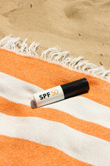 Mineral SPF50 sunscreen stick with UVA + UVB protection on the orange beach towel on the sand near the sea, Beaty routine for healthy skin against sun damage. Vertical
