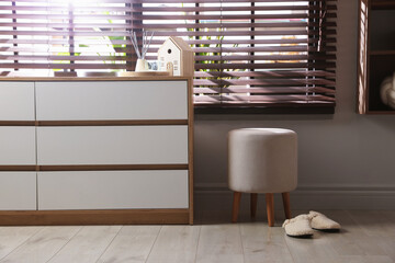 Stylish pouf and slippers near chest of drawers at home