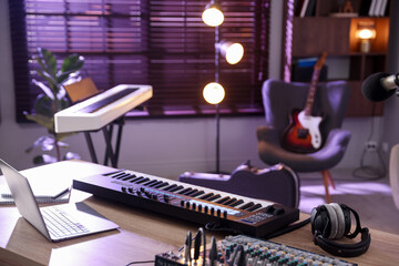 MIDI keyboard, laptop and headphones on wooden table in home studio