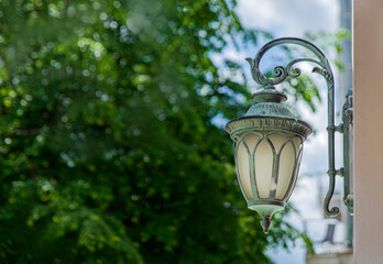 Copper green lantern hanging on wall against green trees
