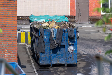 Filled blue dumpster with mixed garbage, on the territory of some factory. Concept of waste...