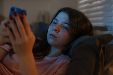 Upset teenage girl with smartphone on bed at night