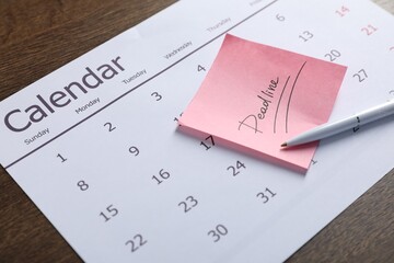 Sticky note with word Deadline, calendar and pen on wooden table, closeup