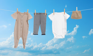 Different baby clothes drying on washing line against blue sky
