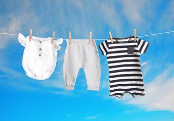 Different baby clothes drying on washing line against blue sky