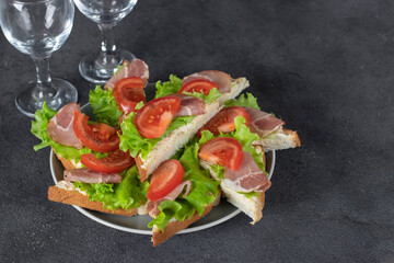 Homemade sandwiches with bacon, tomato and lettuce on white plate on gray background
