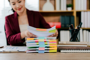Female employee working with pile of documents to search for information and check documents on desk in office. Accounting income, expenses, tax records and hard work.