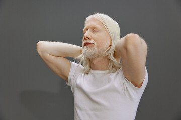 Elderly man relaxing with white hair and beard against a gray background, conveying calmness and...