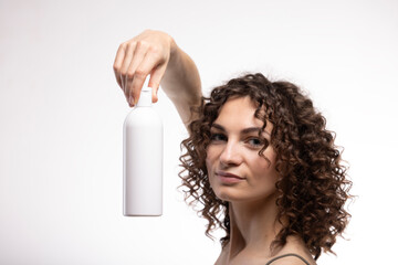 Portrait of an attractive cheerful long-haired curly-haired girl holding a bottle of soap, shampoo,...