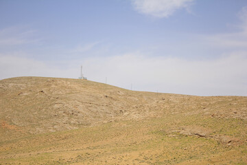 Telecommunications tower standing atop a rocky hill near Yazd, Iran, silhouetted against a clear...