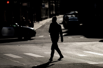 silhouette of pedestrian crossing urban street in dramatic lighting during sunset city traffic...