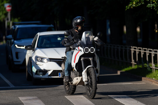 motorcyclist on white adventure bike waiting at pedestrian crossing in city traffic during sunny day with protective gear and helmet urban transportation safety commuting lifestyle road travel - Powered by Adobe