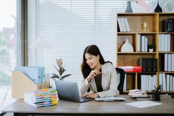 Focused Professional Woman: A smiling young businesswoman efficiently works at her desk,...