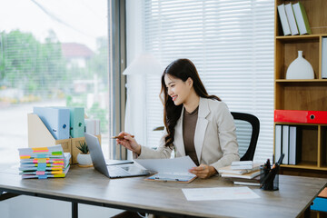 Focused Professional Woman: A smiling young businesswoman efficiently works at her desk,...