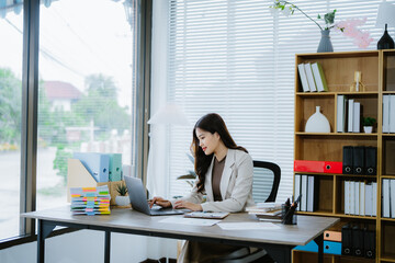 Confident Businesswoman at Work: A smiling young businesswoman confidently works at her desk,...