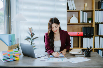 Confident Businesswoman at Work: A smiling young businesswoman confidently works at her desk,...