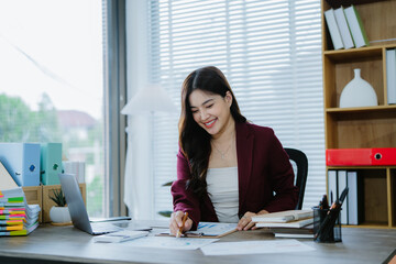 Confident Businesswoman at Work: A smiling young businesswoman confidently works at her desk,...