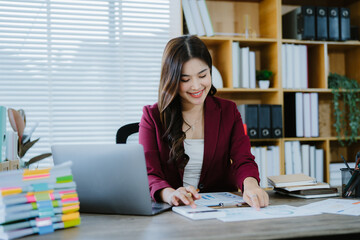 Smiling Asian Businesswoman Working: A young, smiling Asian businesswoman works diligently at her...