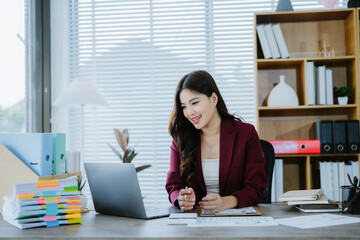 Smiling Asian Businesswoman Working: A young, smiling Asian businesswoman works diligently at her...