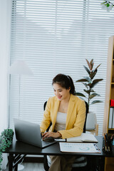 Asian accountant is calculating financial data for a business using a calculator and laptop in her...