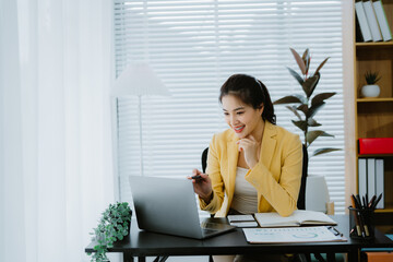 Asian accountant is calculating financial data for a business using a calculator and laptop in her...
