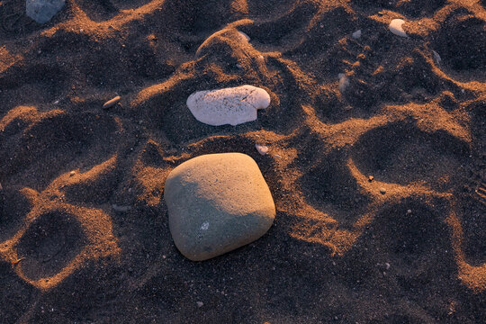 A close-up view of smooth stones resting on a sandy beach. Illuminated by warm sunlight. Making it ideal for themes related to nature, relaxation and coastal landscapes. - Powered by Adobe