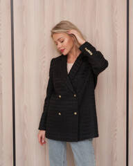 A woman with blonde hair in a black, double-breasted blazer with gold buttons stands, eyes closed,...
