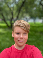 An eleven-year-old guy in a red T-shirt takes a selfie on the street