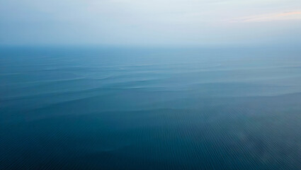 Fototapeta premium An expansive view of a tranquil ocean showcases soft, rolling waves under a pale blue sky during early morning hours, creating a peaceful atmosphere at sea