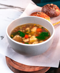Clear Vegetable Soup with Carrots, Cauliflower and Greens in Bowl with Bread on Marble Table