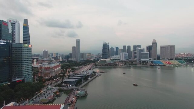 Aerial view of Singapore's Marina Bay at dusk, featuring the HSBC building, Esplanade domes, modern skyscrapers, and boats moving on calm waters.