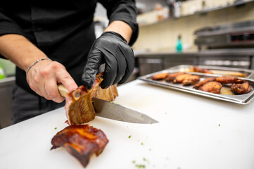 Chef slicing a rack of ribs on a white cutting board in a professional kitchen, wearing black...