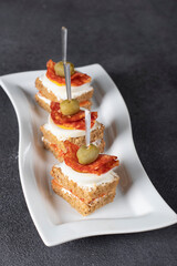 Canapes with salami, egg, olives and kimchi on white plate