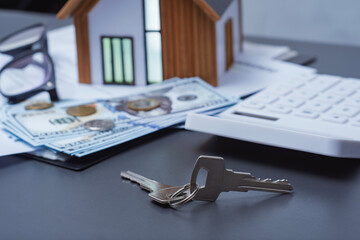 House keys and a stack of dollars with coins and a model house with a calculator. Concept expenses for purchasing a home and financial calculations.