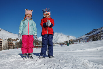 Two children hold scooped snow beneath a clear blue winter sky