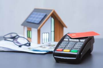 Payment terminal for credit card payment, US dollars and solar powered house model. Concept of property payment and real estate transactions for green housing.