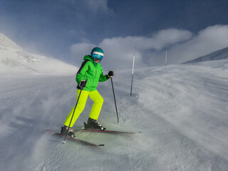Teenage boy in green gear skiing on a snowy windy mountain slope