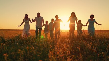 Family of children running on summer field, teamwork. Happy family running on grass in park holding hands. Parents children having fun on field at sunset. Dad, mom, son and daughter together in nature
