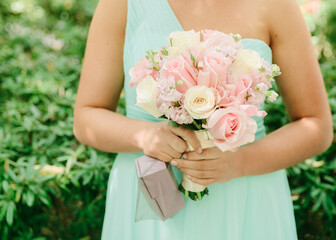 Bridesmaid holding a beautiful bouquet with pastel flowers in a lush garden during a wedding...