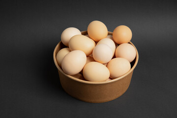 Brown eggs in a paper bowl on dark background – top view
