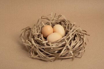 Three brown eggs in paper nest on craft background
