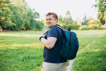 Rear view of blonde man with backpack standing in the countryside. Traveler. Summer time. Portrait of happy young man in casual clothing standing outdoor