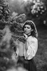 Young pretty caucasian woman in romantic outfit walking in blooming spring garden. Artistic outdoor photo of beautiful red-haired girl posing in fragrant lilac blossom.