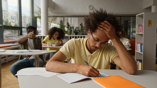 University bully high school bullying college lecture class lesson upset African American guy male man boy student suffer mock laughing classmates diversity students girls guys throw crumpled papers